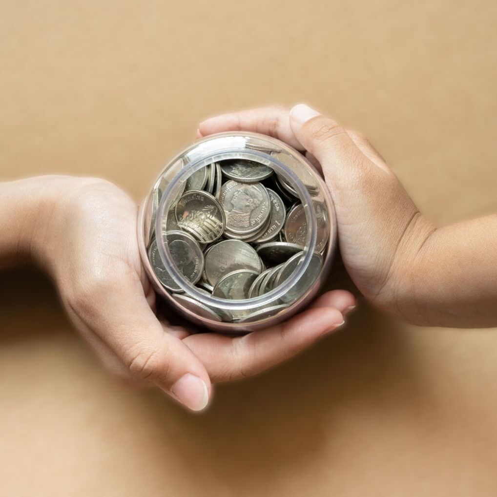 Kid hands holding coins in a jar together as saving concept for family or education. Kid hands holding coins in a jar together as saving concept for family or education. Saving concept using kid hands holding coins.